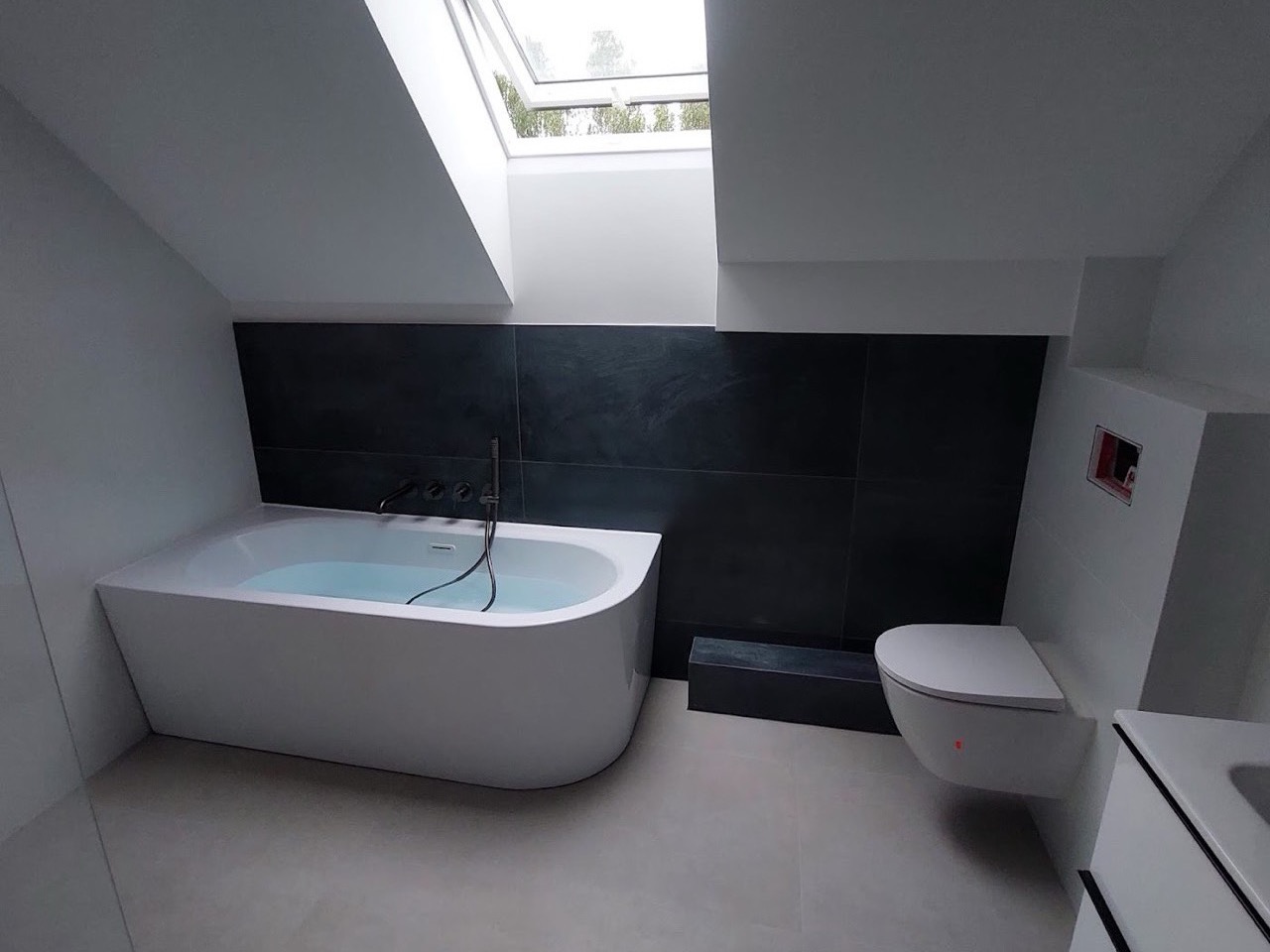 Bad mit freistehender Wanne und dunkler Wand unter dem Dachfenster